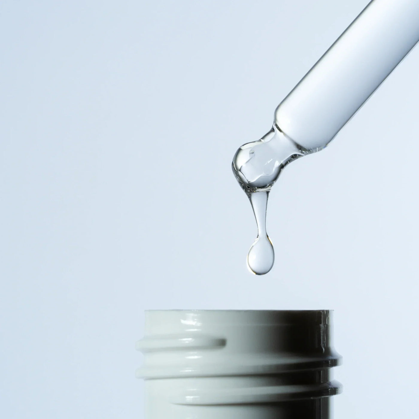 showing a hair product scalp lotion dropper dripping lotion against a white background
