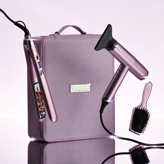 A VODUZ hair styling set in a dusty pink/mauve color, featuring a hair dryer, a flat iron, a brush, and a matching carrying case on a light pink background.